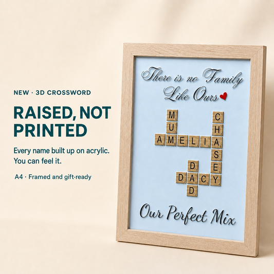 Personalized wooden framed crossword plaque on a light beige background. The light blue insert features a crossword made of wooden Scrabble tiles spelling family names, with silver script text reading 'There is no Family Like Ours' and 'Our Perfect Mix'.