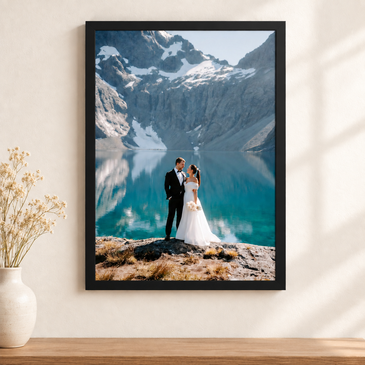 A2 framed photo print of a wedding couple by an alpine lake, black frame, hanging on a white wall above a wooden shelf