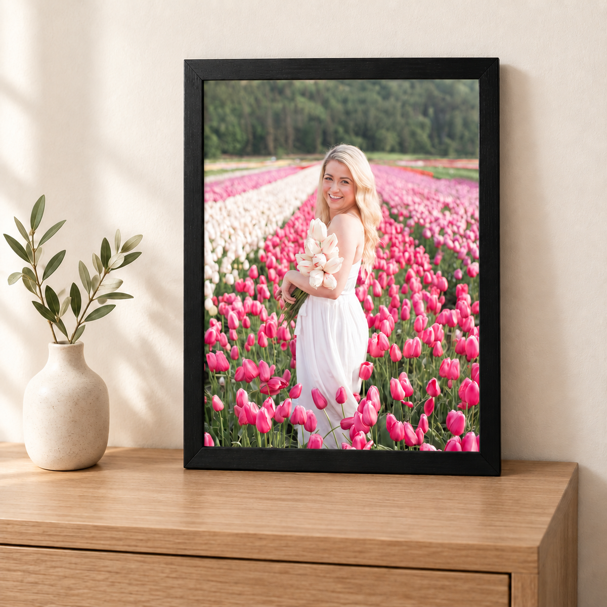 A4 framed photo print of a woman holding tulips in a flower field, black frame, displayed on a wooden sideboard next to a small vase